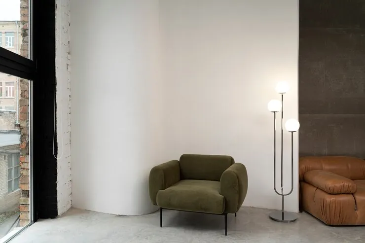 Cameră minimalistă cu pereți albi, un fotoliu verde, o lampă de podea și o banchetă din piele
